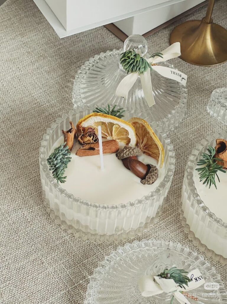 Handmade spice candle in a decorative glass jar, featuring dried orange slices, cinnamon sticks, and acorns.