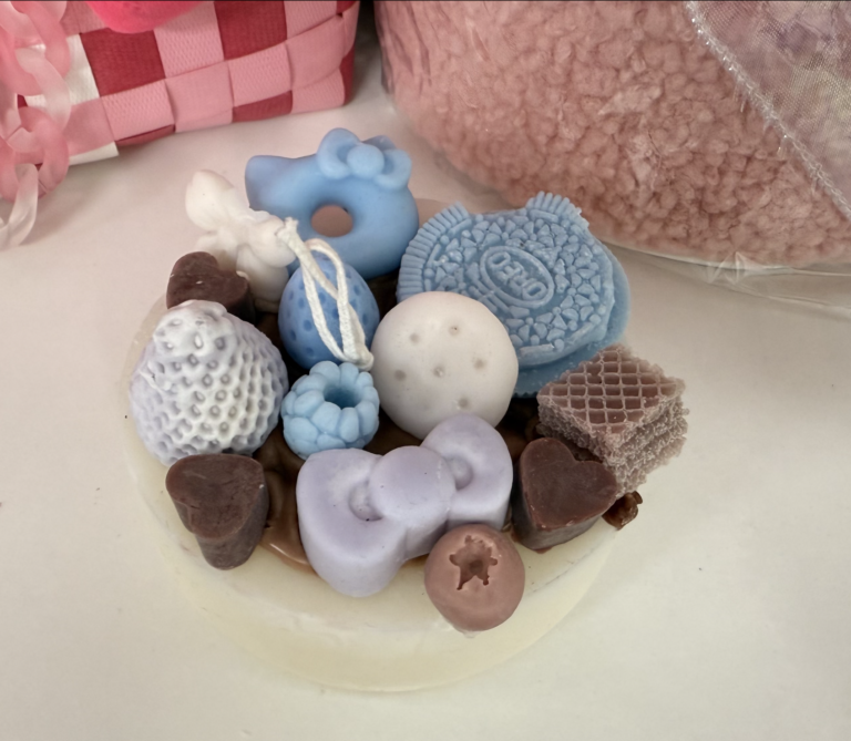 Handmade birthday cake candle decorated with wax designs resembling cookies, hearts, and berries in pastel colors.