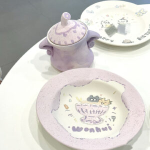 Adorable hand-painted ceramic plates and jar in pastel purple tones, featuring personalized cartoon-style art and names.