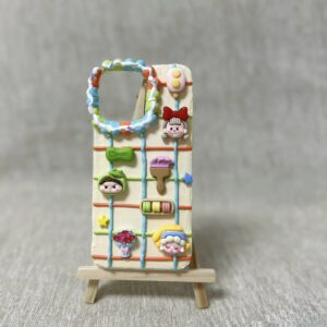 A handcrafted 3D phone case with a cream and pastel color palette featuring playful miniatures of cartoon characters, sweets, and decorative elements arranged in a grid pattern.