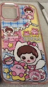 A cute and colorful phone case featuring an illustrated girl in a white hood, surrounded by pink Kirby characters, candy elements, and plush toys on a pastel background.