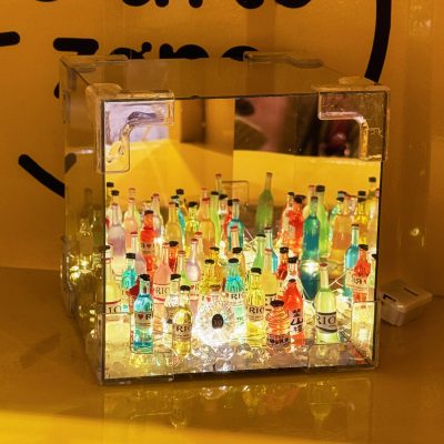 A creative LED display featuring miniature colorful liquor bottles inside a mirrored acrylic box, reflecting a vibrant and illuminated aesthetic.