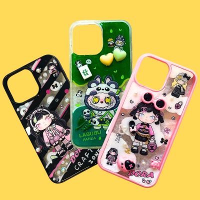 Three colorful DIY phone cases with cartoon characters and embellishments on a yellow background.