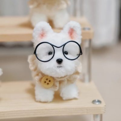 A handmade plush dog figurine wearing glasses and a cute buttoned scarf, displayed on a wooden shelf.
