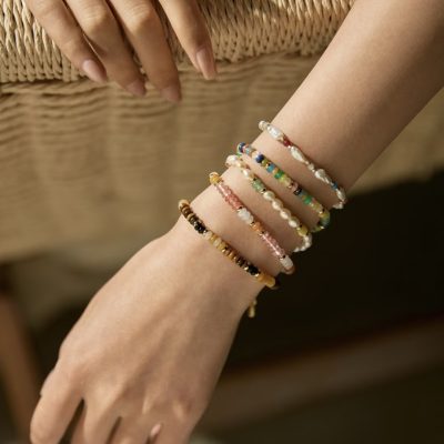 A hand wearing a stack of colorful handmade beaded bracelets featuring pearls, crystals, and natural stones.