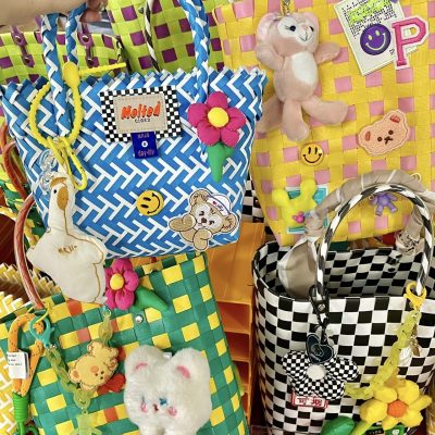 A collection of colorful woven DIY bags decorated with plush toys, smiley face patches, flowers, and creative keychains