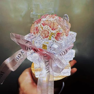 Crystal rose night light made from clear acrylic blocks and pink roses, sitting on a wooden base with LED lighting and a pink ribbon tied around it.
