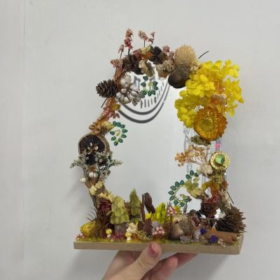 A handmade dry flower mirror decorated with preserved blooms, pinecones, and natural elements for a whimsical and artistic look